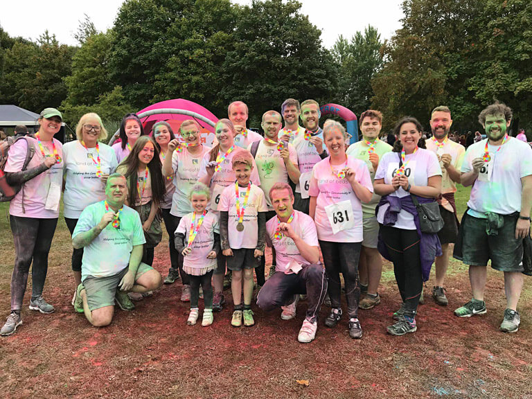 Several Land of Beds staff members together smiling, proudly holding their medals after completing a charity Colour Run event