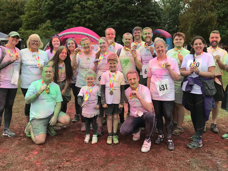Land of beds team holding colour run medals