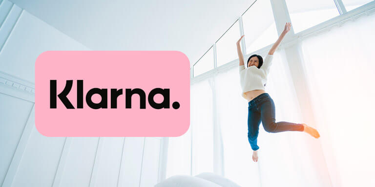 Woman jumping for joy on a bed next to the Klarna logo
