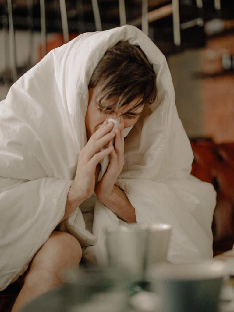 Man wearing a duvet while blowing his nose due to allergies