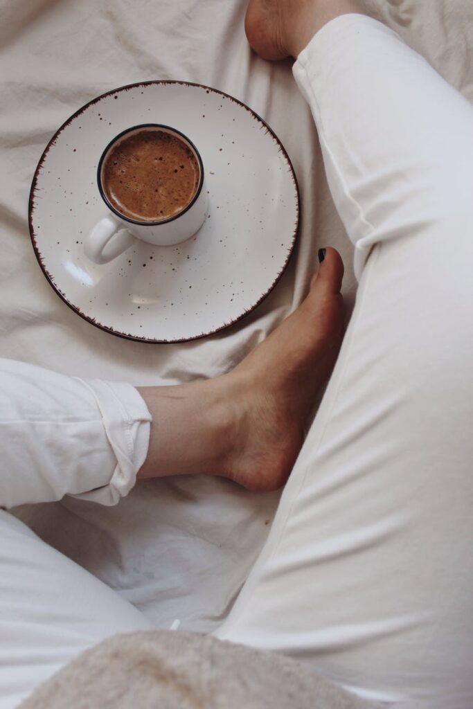 Coffee with saucer next to bare feet on a bed