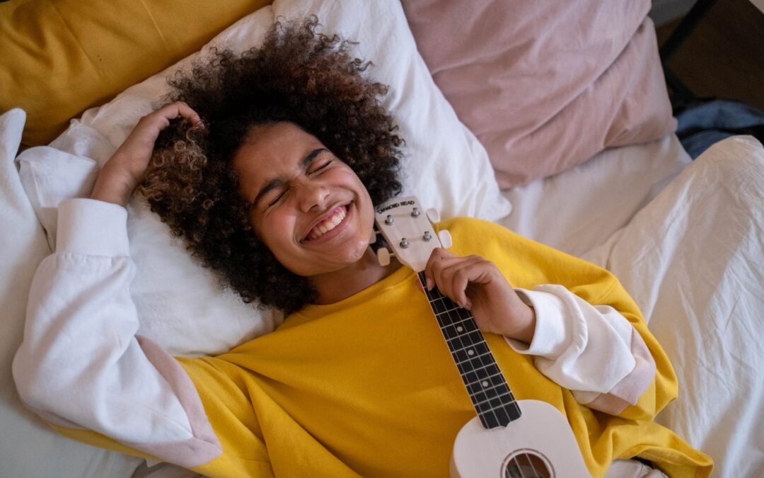 Boy with guitar enjoys many colourful pillows on a bed