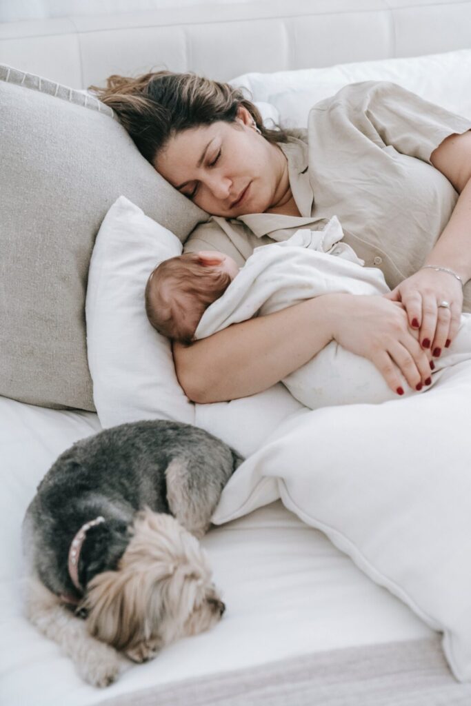 Woman sleeping in bed while clutching her baby. Her dog sleeps nearby