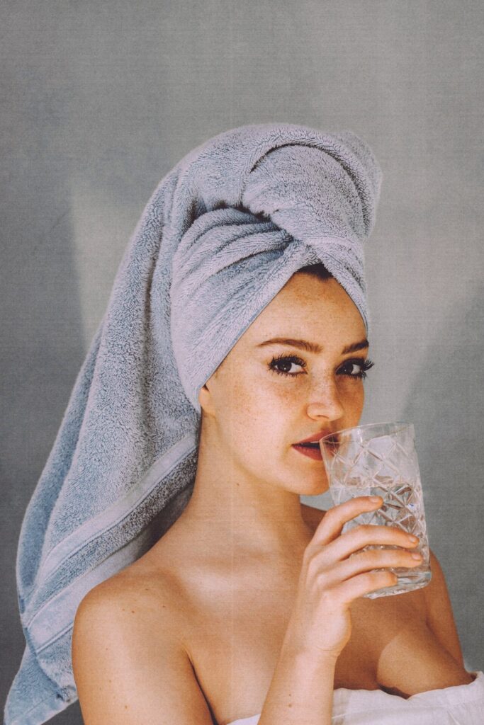 woman with towel on her head drinking water so the hydration will help her get to sleep quickly