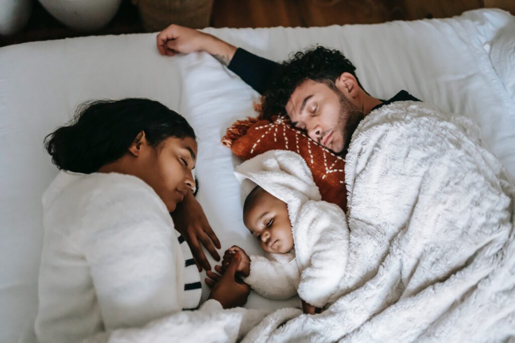 Young parents asleep on a bed with a baby between them