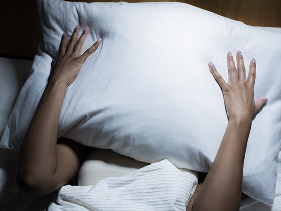 A woman holding a pillow to her face as she finds the first stage of sleep frustrating