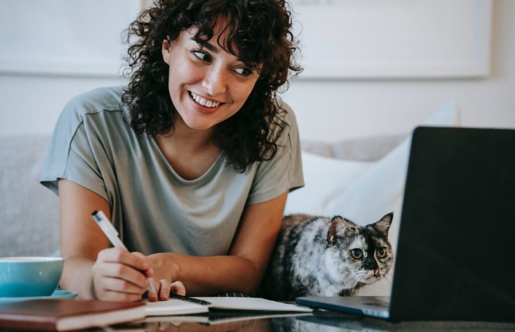 Woman working from home on her laptop as her cat takes an interest in the screen