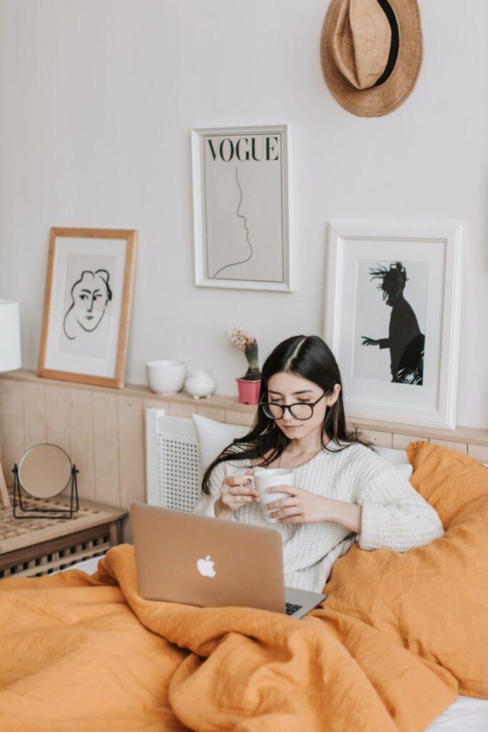 Woman working from home on her laptop in bed, cradling a cup