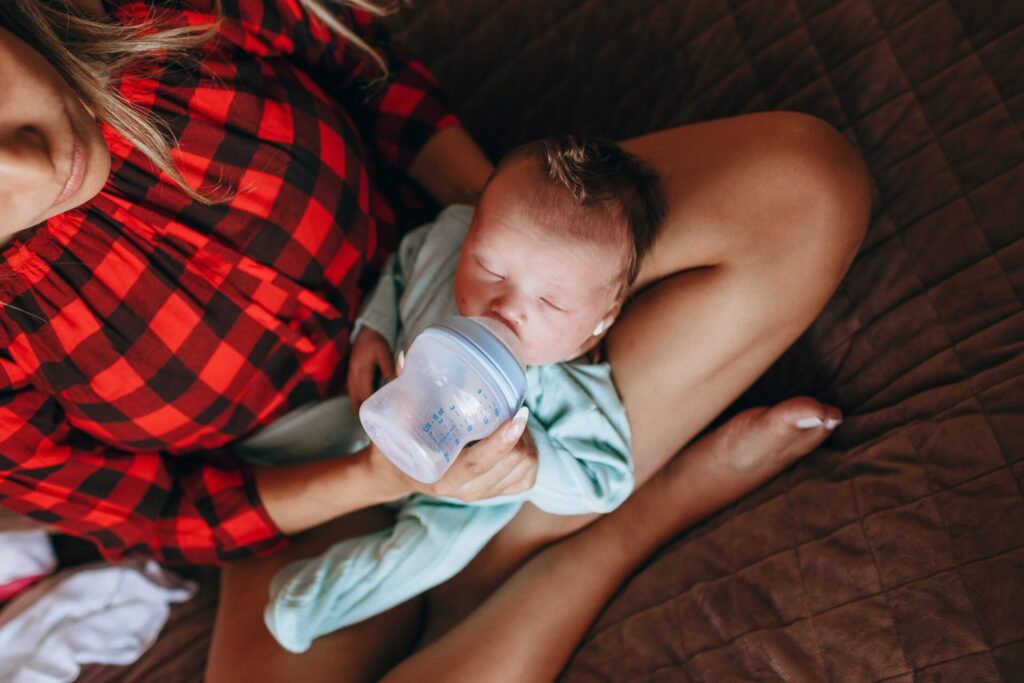 Mother managing her baby's sleep by feeding him a bottle as he lays on his mother's bare legs