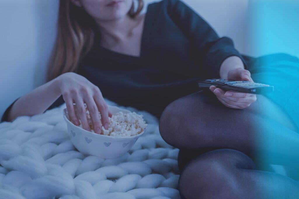 Woman enjoying hygge living by lying on bed snacking on popcorn