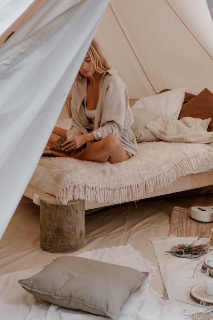 Woman in cream coloured hygge tent sitting on a bed reading a book