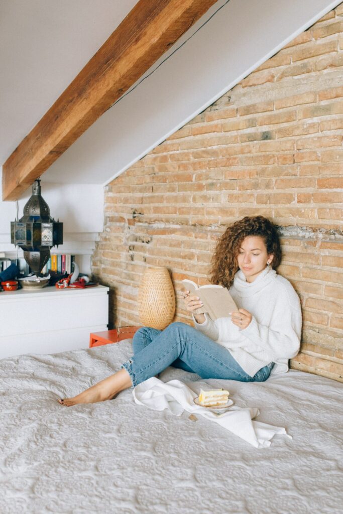 Woman enjoying hygge living sat on her bed in a loft against a brick wall
