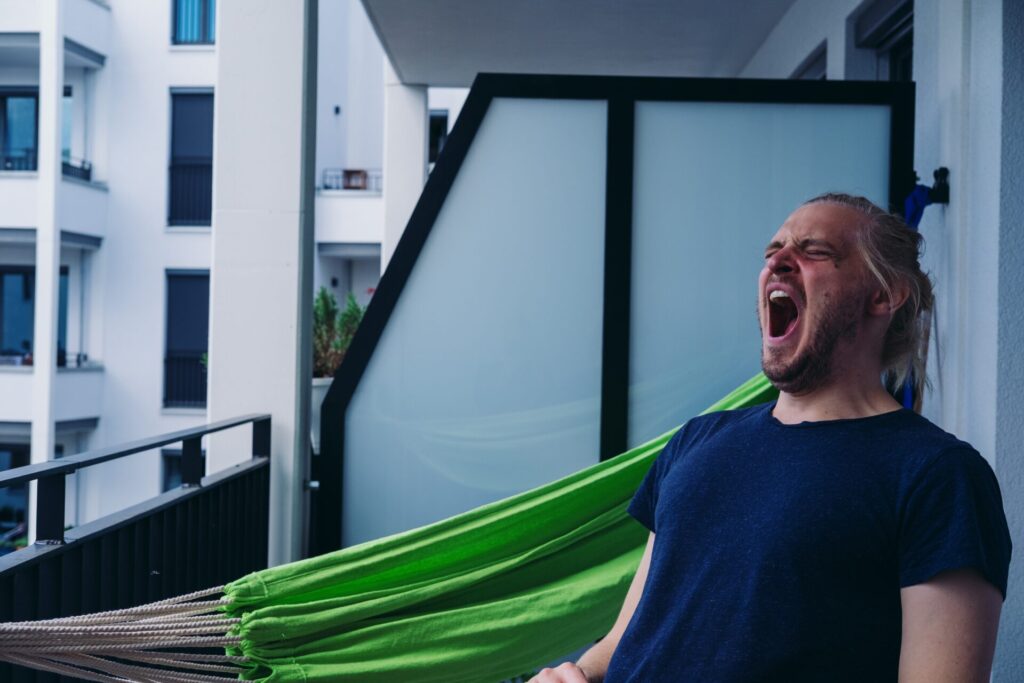 A man sat on a balcony with his mouth wide open, yawning