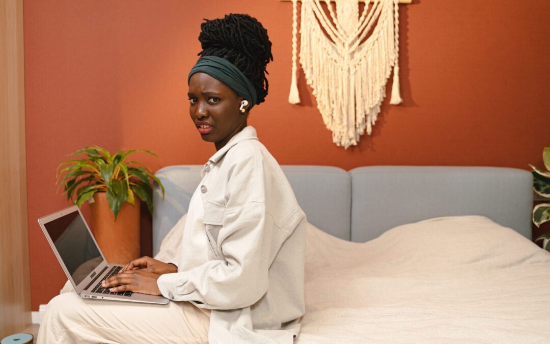 Unhappy woman sitting on edge of bed with laptop