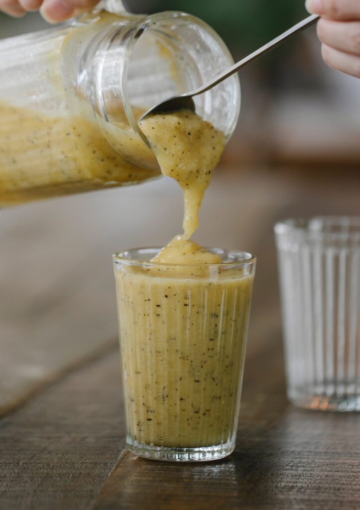 Banana smoothie being poured from a jug into a glass, a spoon helping tease it out