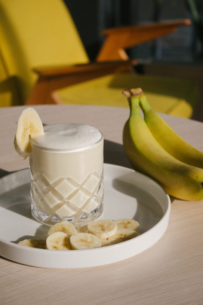 An inviting glass of thick, creamy banana smoothie with a couple of bananas next to it