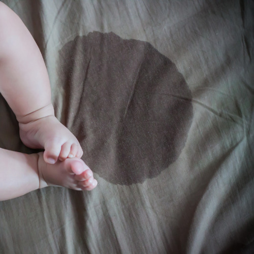 A wet patch on a bed sheet next to baby's feet