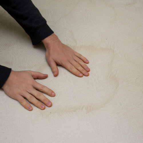 A water stained mattress being rubbed by a pair of hands