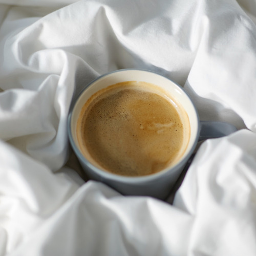 A cup of coffee sits in the middle of some bed sheets