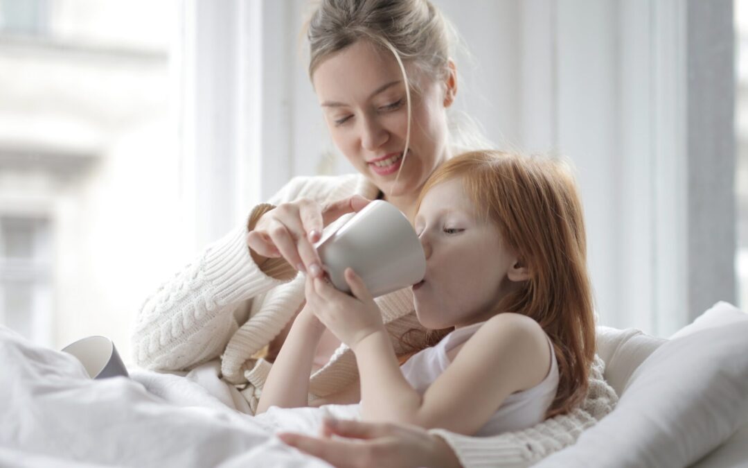 Ginger girl being helped to sip coffee in bed by her mother