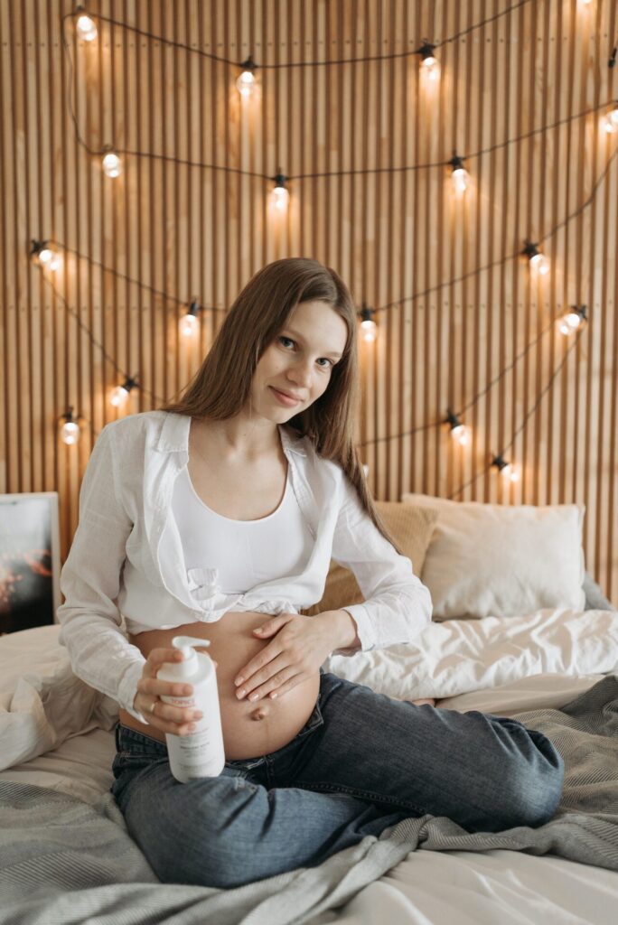 A pregnant woman rubbing cream on her belly as she sits in bed