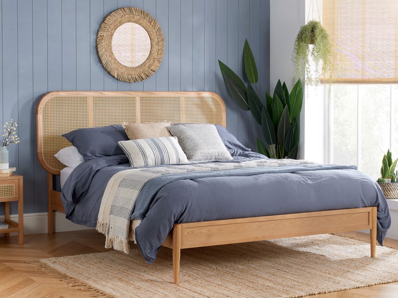 Blue bedroom with a wooden bed, cane headboard, layered blue bedding and indoor plants