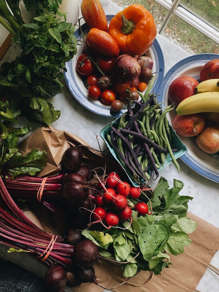 Fresh vegetables and fruit arranged on a kitchen counter, including tomatoes, peppers, beans, beetroot and herbs