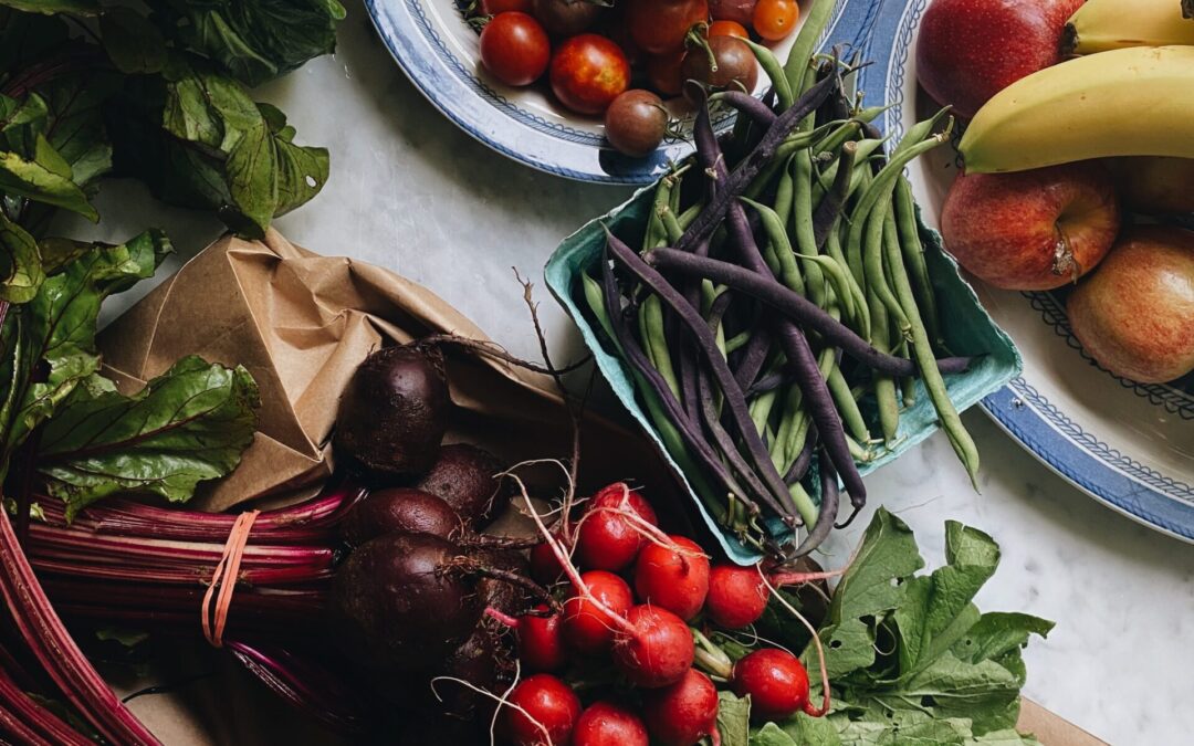 Fresh vegetables and fruit arranged on a kitchen counter, including tomatoes, peppers, beans, beetroot and herbs