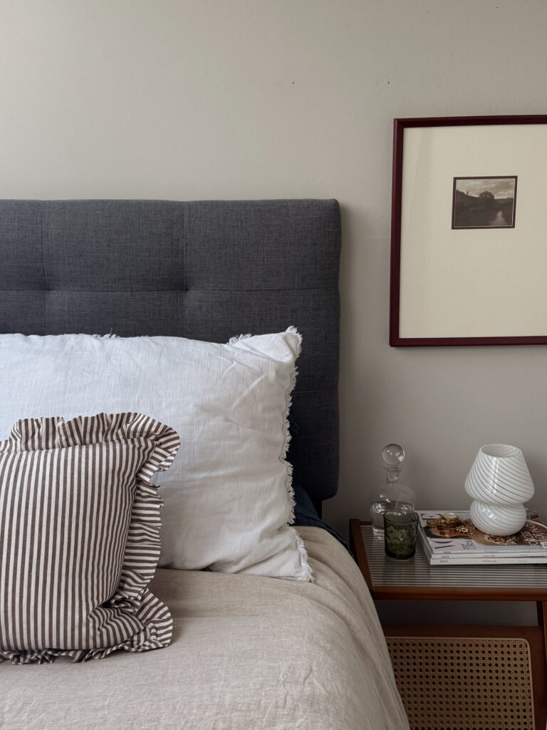 Neutral bedroom with upholstered headboard, layered white bedding and a styled bedside table