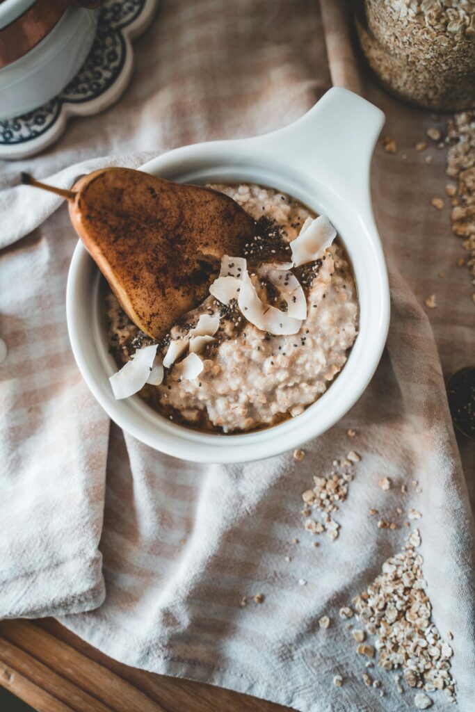 Bowl of porridge topped with sliced pear, coconut flakes and seeds on a neutral table setting