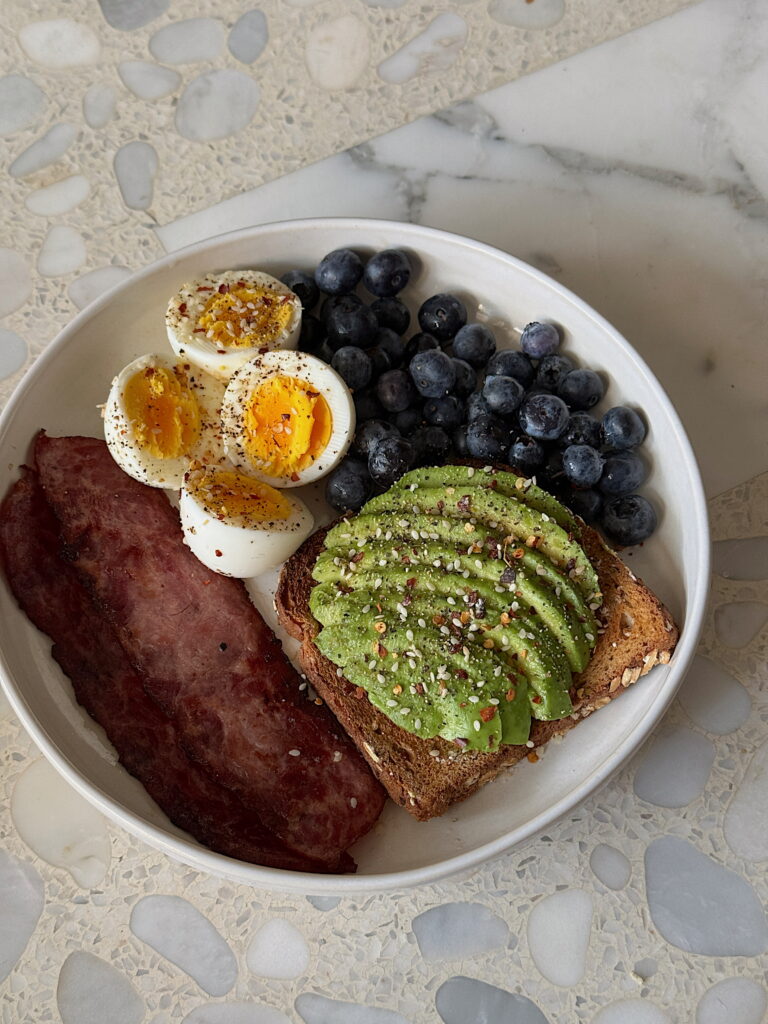 Balanced breakfast with avocado toast, boiled eggs, bacon and blueberries served in a bowl