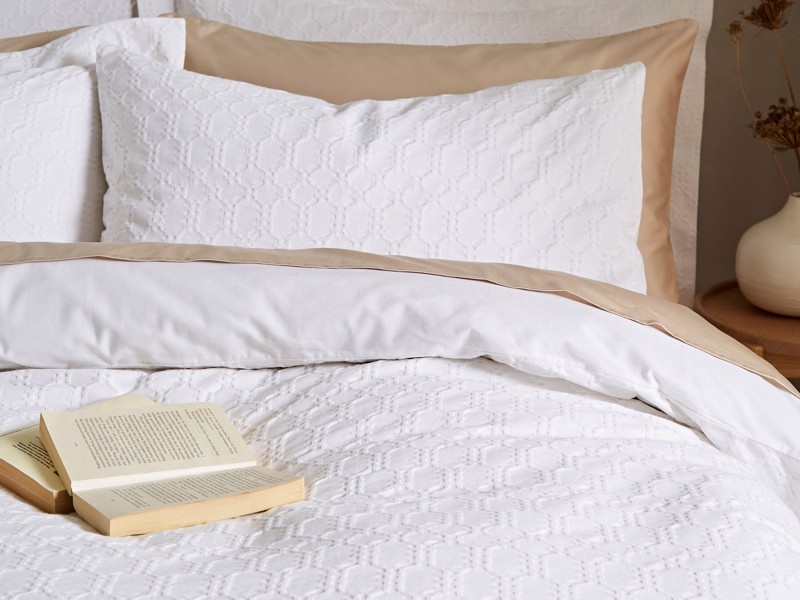 White textured bedding layered with neutral beige pillowcases on a calm, minimal bed