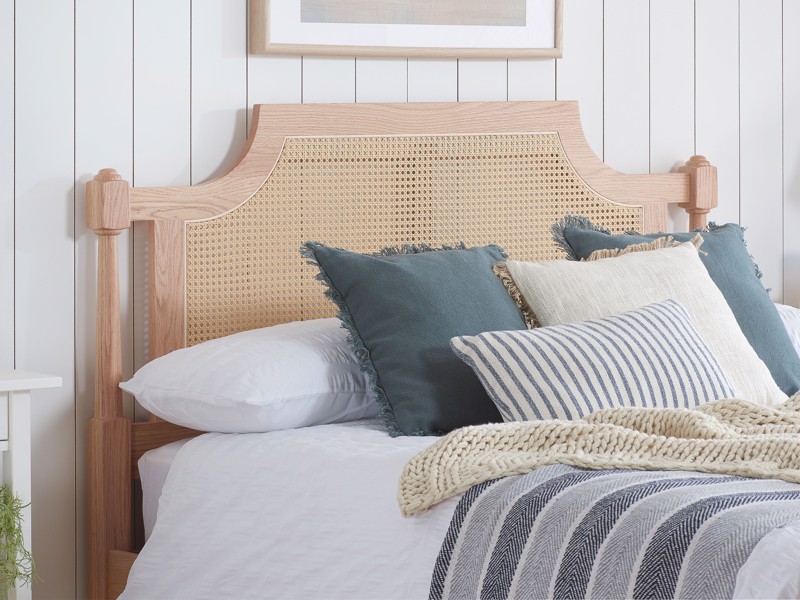 Wooden bed with a cane headboard, layered white bedding and blue accent cushions