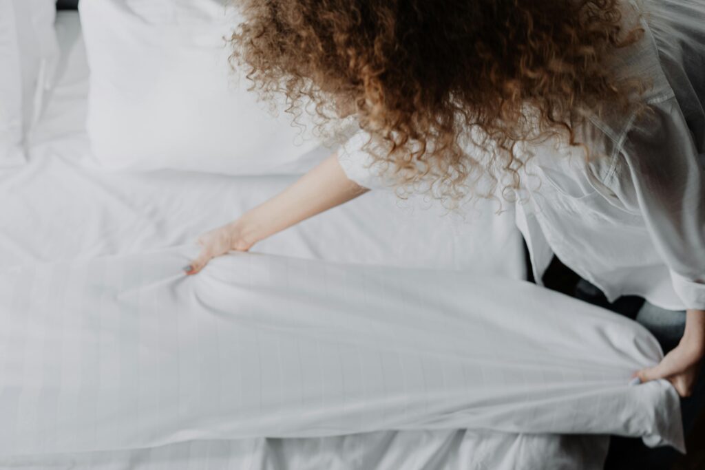 Close-up of a neatly made bed with soft white pillows and rumpled white bedding against a dark upholstered headboard, lit by gentle natural light for a calm, minimal bedroom feel