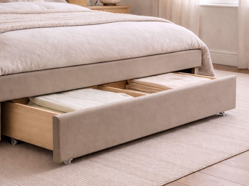 Taupe upholstered bed frame with pull-out storage drawer underneath showing folded bedding