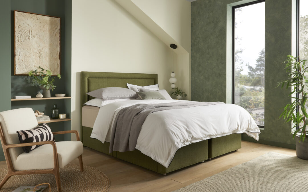 Green upholstered divan bed with matching headboard in a Japandi-style bedroom with neutral bedding, wooden flooring, and natural light