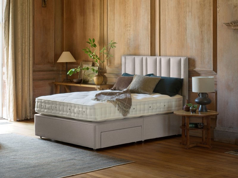 Upholstered divan bed with tall padded headboard and storage drawer in a warm wood-panelled bedroom interior