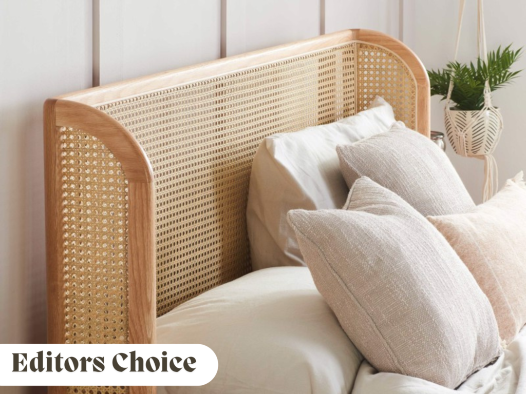 Neutral rattan bed frame with white and cream bedding and a plant in the background