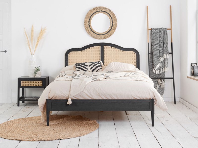 Black wooden bed frame with rattan headboard in a minimalist bedroom with light flooring and natural textures