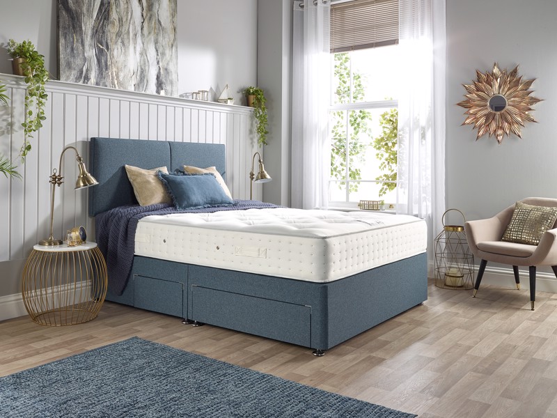 Blue upholstered divan bed with storage drawers and mattress in a bright, modern bedroom with soft natural light